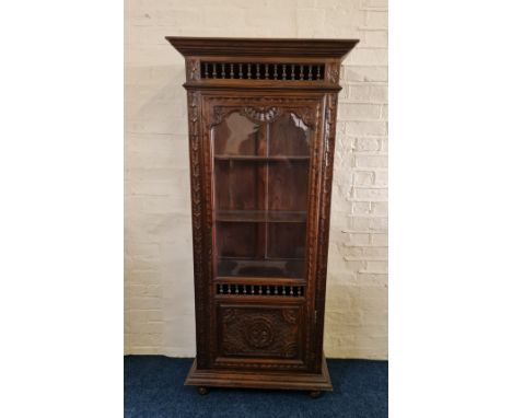 An oak single glazed door display cabinet with turned open gallery and carved panel to base. IMPORTANT: Online viewing and bi