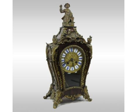 A 19th century rosewood cased and brass mounted mantel clock, the bombe cut brass case surmounted by a figure, having a white