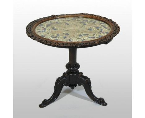 A 19th century carved rosewood occasional table, the circular top inset with a Chinese woolwork panel, having raised scrolled