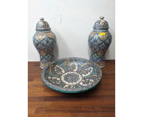Two Moroccan lidded urns with a large dish all decorated with greens, yellows and blues with silver coloured typingLocation: 