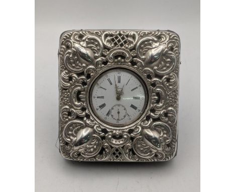 An early 20th century white metal open faced keyless pocket watch with a silver mounted bedside case having floral embossed d