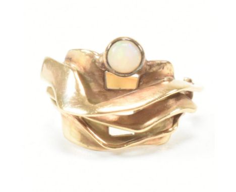 A hallmarked 9ct yellow gold and opal ring. The ring having an undulating brutalist head bezel set with a round cut opal cabo