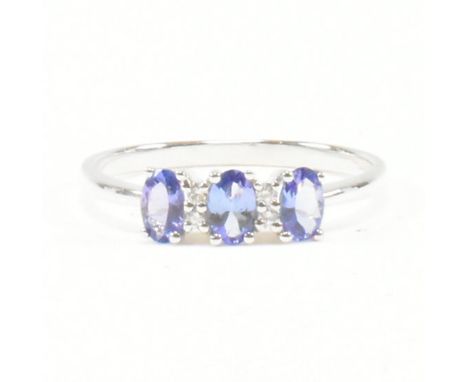 A hallmarked 14ct white gold tanzanite and diamond ring. The ring having three oval cut tanzanite flanked by accent diamonds 