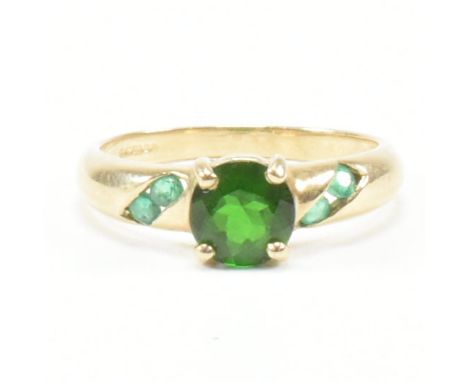 A hallmarked 9ct yellow gold, emerald and diopside ring. The ring having a central round cut diopside flanked by two channel 