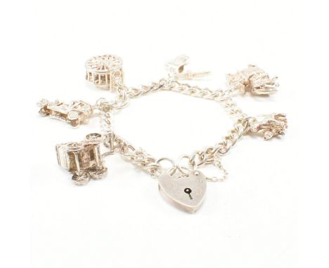 A vintage silver charm bracelet with charms. The chain comprised of uniform curb links united by a heart padlock clasp, marke