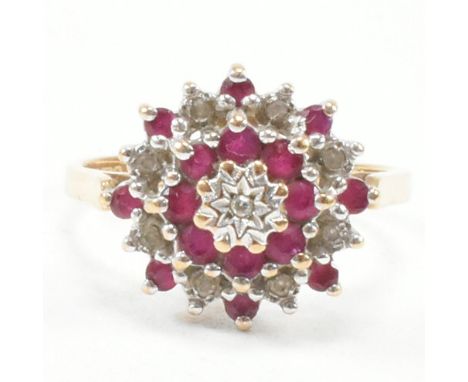 A hallmarked 9ct yellow gold, diamond and ruby cluster ring. The ring having a central round cut illusion set diamond encompa