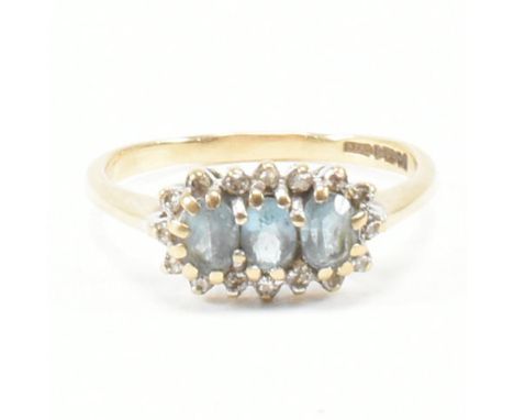 A hallmarked 9ct yellow gold, topaz and diamond cluster ring. The ring having three oval cut blue stones encompassed by a hal