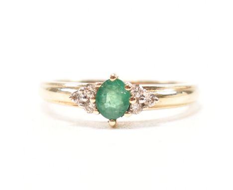 A hallmarked 9ct yellow gold emerald and diamond ring. The ring having a central oval cut emerald flanked by a trio of round 