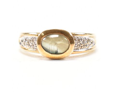 A hallmarked 9ct yellow gold, chatoyant gem and diamond ring. The ring having a bezel set oval cabochon of green blue cats ey