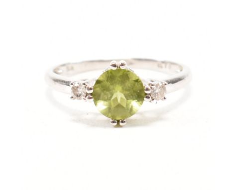 A hallmarked 9ct white gold, peridot and diamond ring. The ring having a round cut double prong set vibrant green stone flank