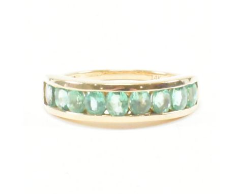 A hallmarked 14ct yellow gold and emerald nine stone ring. The ring having nine oval cut channel set green stones to a tapere
