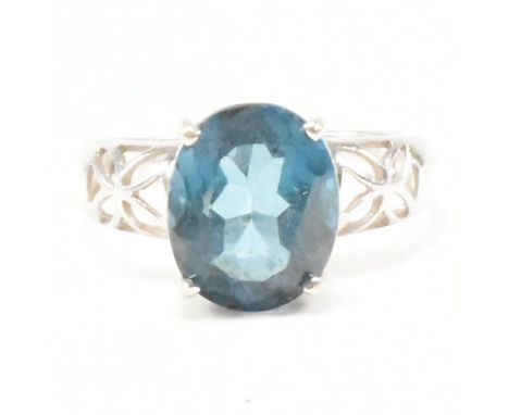 A hallmarked 9ct white gold and topaz dress ring. The ring having an oval cut prong set blue stone to pierced shoulders on a 