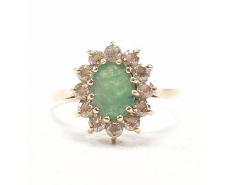 A hallmarked 9ct yellow gold, emerald and white stone halo dress ring. The ring having an oval cut emerald encompassed by a c