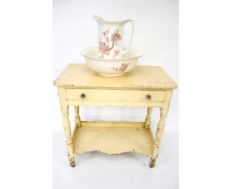 A painted pine wash stand and a wash bowl and pitcher. The wash stand with a single drawer and an undertier, on casters, H73c