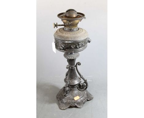 A late Victorian cast metal pedestal oil lamp, the font having a frieze of lion masks and flowers on inverted stem supported 
