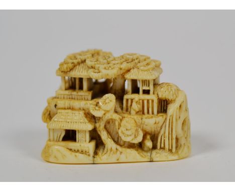 A Japanese ivory netsuke, Meiji period, carved as figures and buildings in a rocky landscape, signed, 3.5cm wide