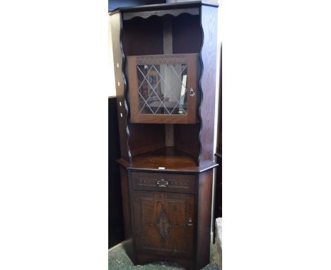 A Newplan oak corner display cabinet, rounded cornice with shaped apron above a shelf and glazed door, the protruding base wi