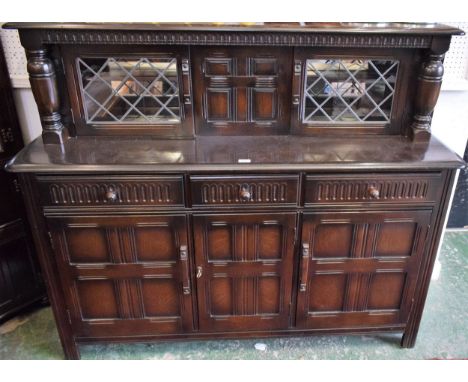 A Priory oak style duodarn, rounded rectangular top above a pair of glazed doors enclosing a mirror back and shelf, the protr