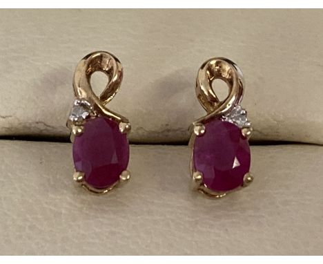 A pair of 9ct gold ruby and diamond stud style earrings with gold twist design. Each earring set with an oval cut ruby and a 