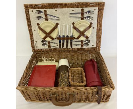 A large vintage wicker picnic basket complete with cutlery, plates and cups. Basket also includes a red plastic sandwich box,