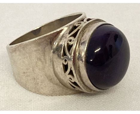 A modern design silver statement dress ring set with a large amethyst round cut cabochon. Floral pierced work to mount. Insid