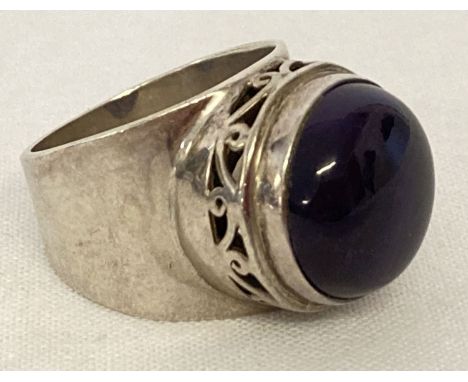 A modern design silver statement dress ring set with a large amethyst round cut cabochon. Floral pierced work to mount. Insid