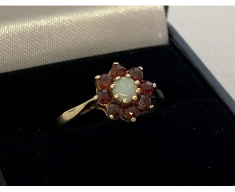 A 9ct gold, flower design garnet and opal dress ring. Central round opal surrounded by 8 round cut garnets. Fully hallmarked 