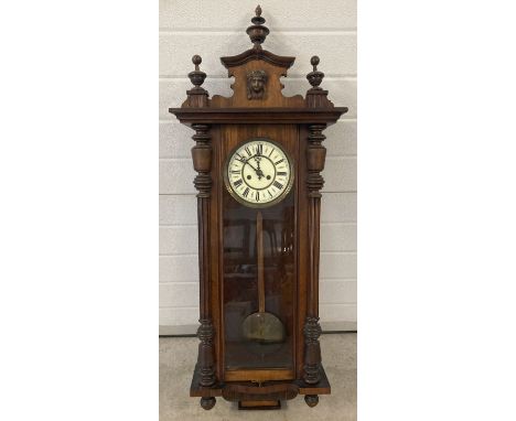 A Victorian German wooden cased wall hanging clock with carved wooden plinth and finial decoration. With enamel face, pendulu