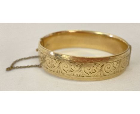 A vintage 9ct gold with metal core hinged bangle with half floral decoration and safety chain. With push clasp. Marked to ins