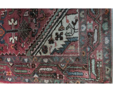A GOOD ORIENTAL WOOL RUG the light pink ground with central panel filled with palmets, lozenges and hooks within a conforming