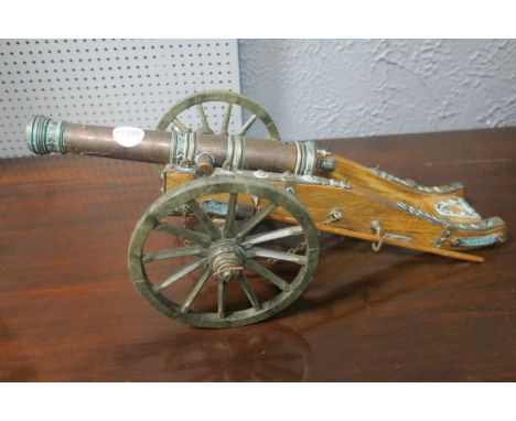 A WOODEN FRAMED AND GILT MINIATURE METAL MODEL OF A CANNON with circular wooden carved wheels fitted with brass clock engrave