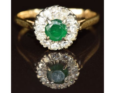 An 18ct gold ring set with a round cut emerald surrounded by diamonds in a platinum setting, 3.6g, size R