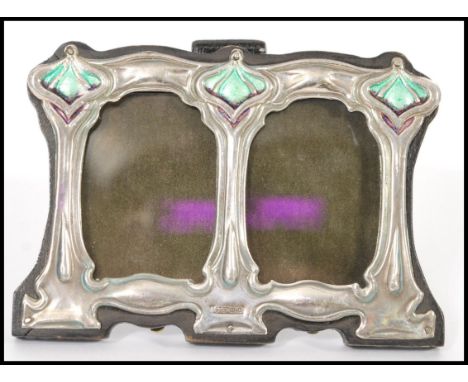 A Liberty / Art Nouveau style double picture frame with sterling silver decoration to the front with green enamelled panels o