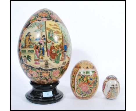 A group of three vintage 20th century Japanese ceramic eggs to include a large example on ebonised wooden base and two smalle