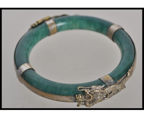 A 19th century Chinese jade bangle. The deep green jade bangle having silver white metal dragon mounts. Weighs 59 grams.