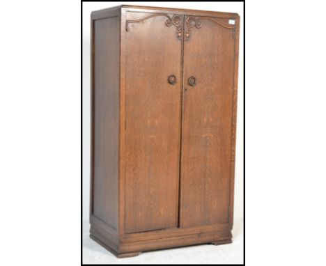 A 1930's Art Deco oak bachelors wardrobe with full length panel door having central embellishment. The door opening to reveal