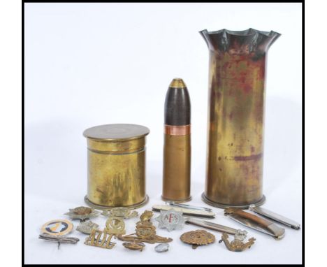 A group of military related items to include various pen knives, cap badges and two artillery shell trench art pieces includi