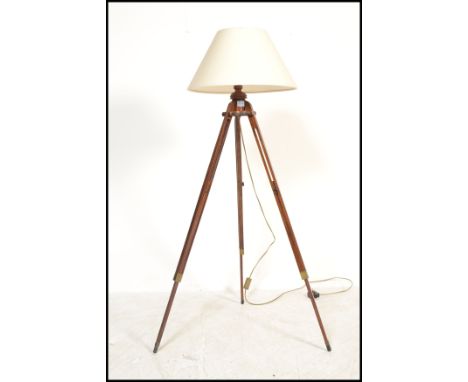 A contemporary tripod standard lamp being raised on a mahogany folding stand complete with the shade atop, believed to be fro