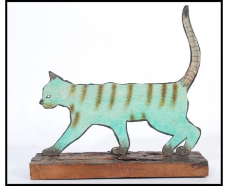A vintage 20th century folk art painting on metal sculpture of a cat being raised on a live edge wood base.
