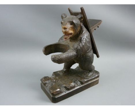 A CARVED BLACK FOREST BEAR TAPER HOLDER & MATCHBOX STAND formed as a standing bear, arms outstretched with shelved board stra