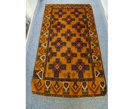 A BALUCHI WOOLLEN RUG, rust ground with cross patterned central panel and repeating running border, 177 x 97 cms