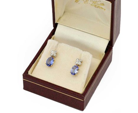 A pair of tanzanite and diamond drop earrings, a white x-shaped motif set throughout with eight-cut diamonds suspends an oval