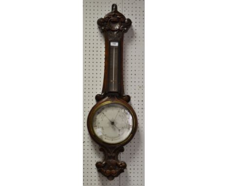 A late 19th/early 20th century carved oak aneroid barometer thermometer, white barometer dial, brass temperature scale, scrol
