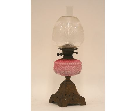 A Victorian oil lamp, raised on ornate cast iron base with cranberry and pink tinted opaque glass font and etched glass shade