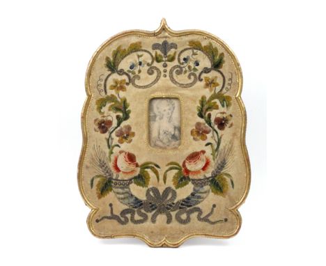 A late 18th Century needlework easel frame, of swept outline with giltwood edge, enclosing a panel of cream velvet worked in 