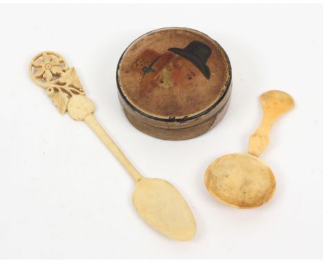 A papier mache image snuff box and two bone spoons, the circular box with a head and shoulders male figure wearing a hat whic