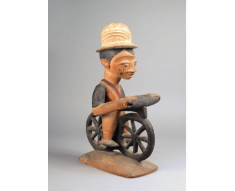 A Yoruba cyclist Nigeria carved from one piece, wearing a pith helmet, a sash and shorts, with painted decoration, on a recta