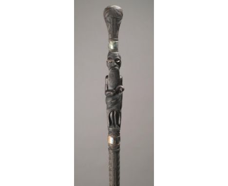 A Maori cane New Zealand with haliotis shell, carved a standing chief with a tattooed face and with a long beard and holding 