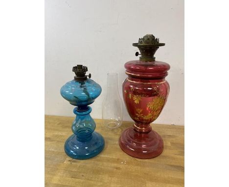 A blue glass oil lamp with white enamel floral decoration, measures 28cm high along with a cranberry glass oil lamp (2)