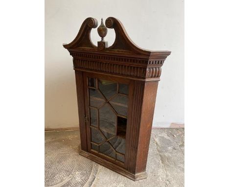 A George III oak hanging corner cabinet, late 18thc, swan neck pediment with turned finial over dental cornice and acanthus c